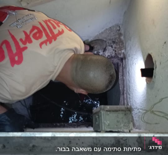 אדם מתכופף מעל פתח ביוב עם פנס